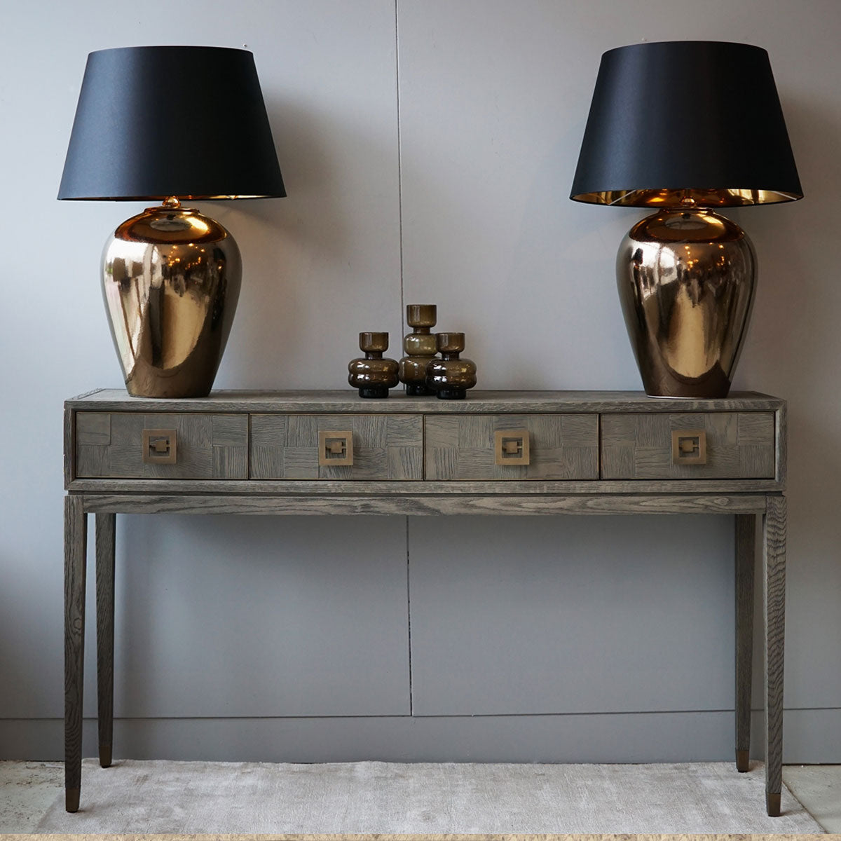 Two gold table lamps with black shades on a wooden console against a gray wall.