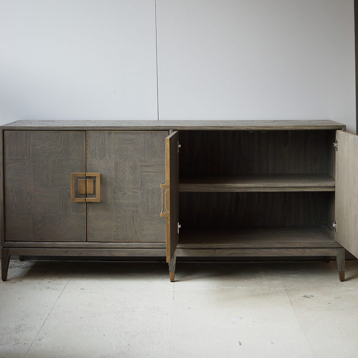 Oak wood sideboard with open door on a white floor and light gray wall background