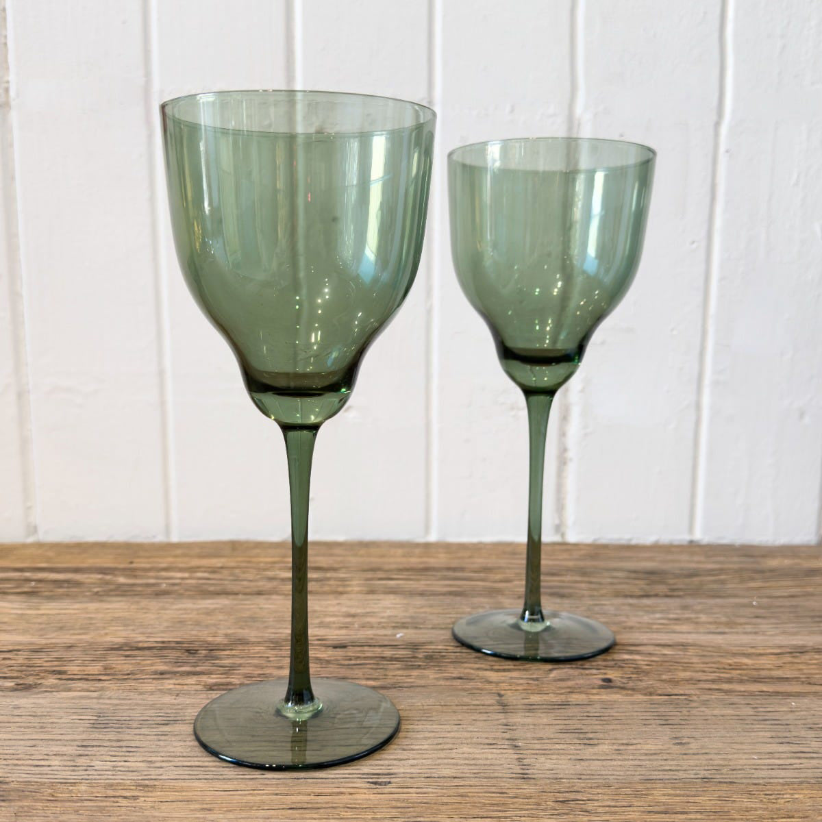 Two olive green gin glasses with a long stem, displayed on a wooden surface against a white background.