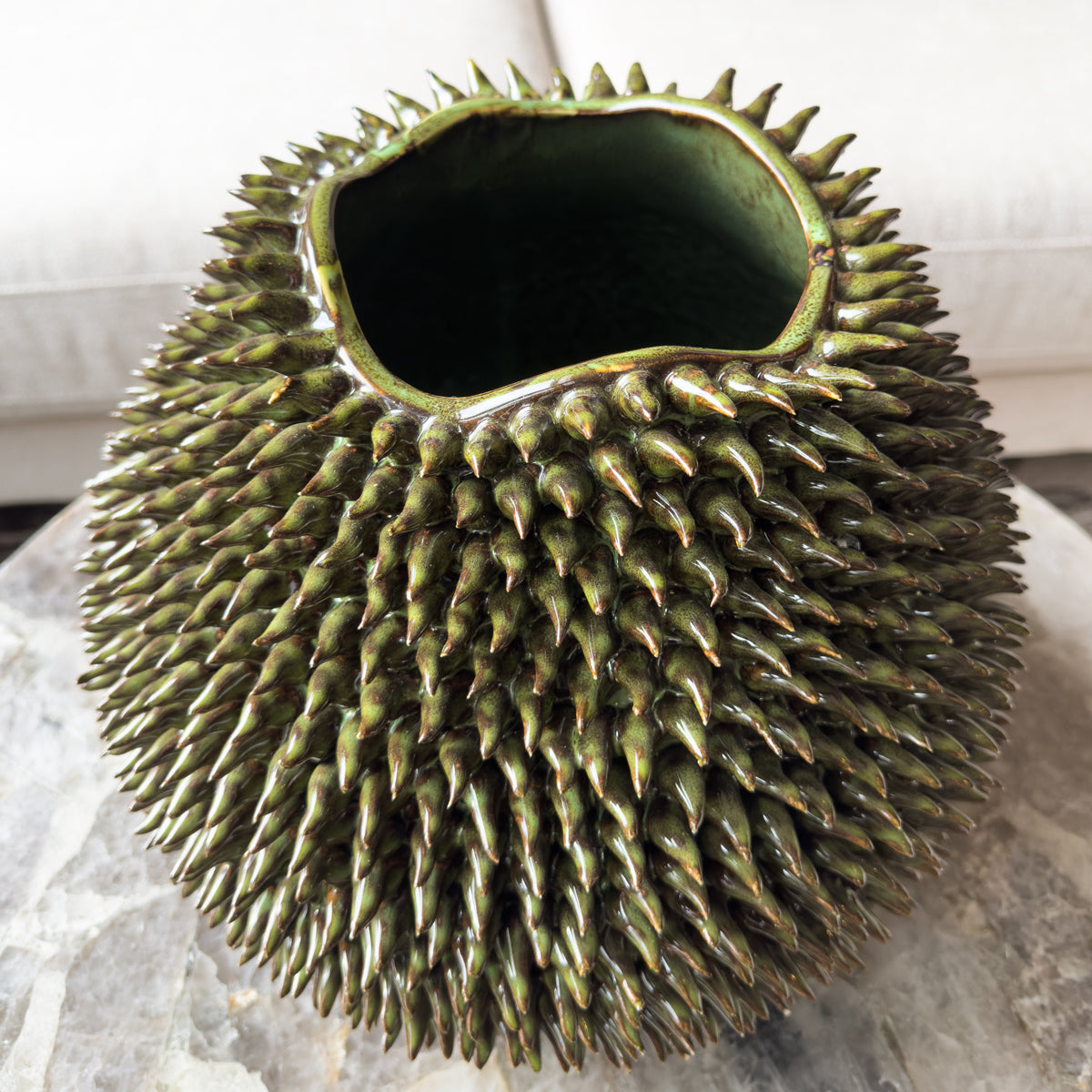 A green urchin style vase, which is covered in green spikes, sitting on a quartz coffee table.