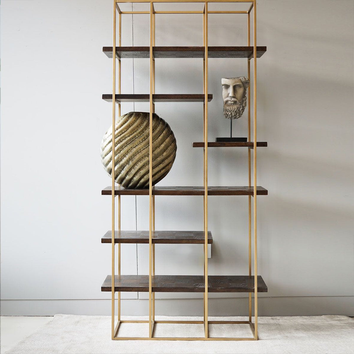 Modern bookshelf with gold frame and wooden shelves against a plain wall.