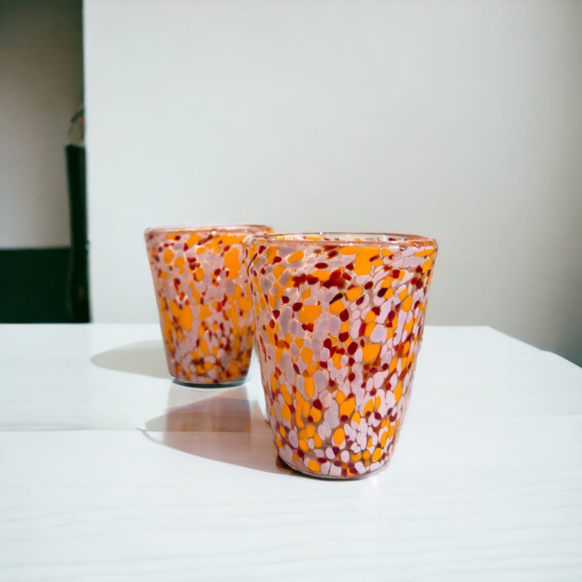 Two colorful glass tumblers on a white surface with a neutral background