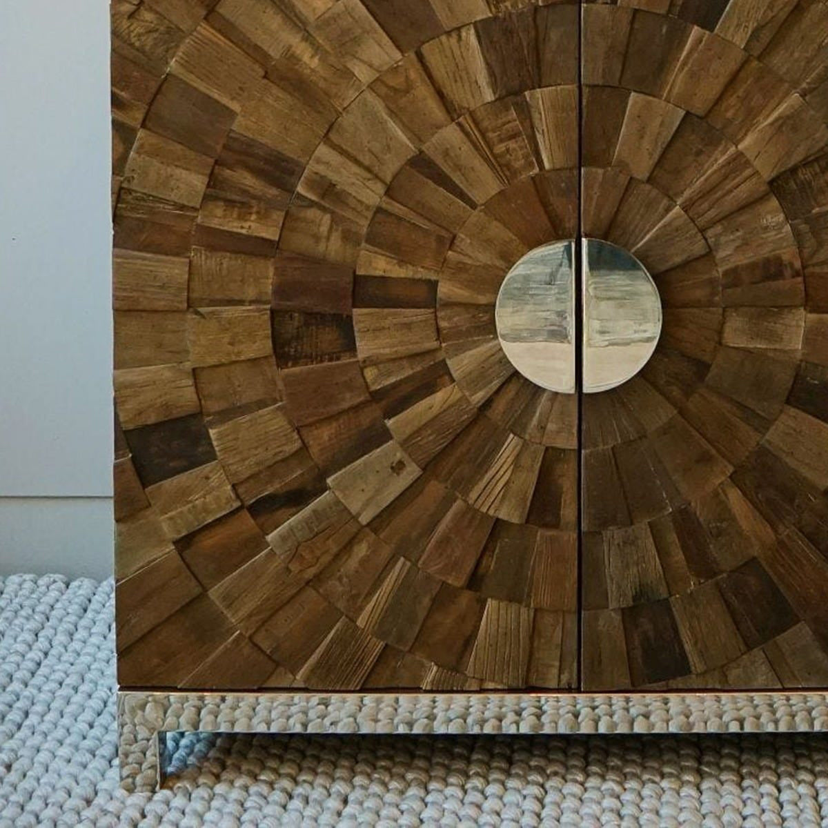 Wooden cabinet with a circular design and mirrored circular handle on a textured surface