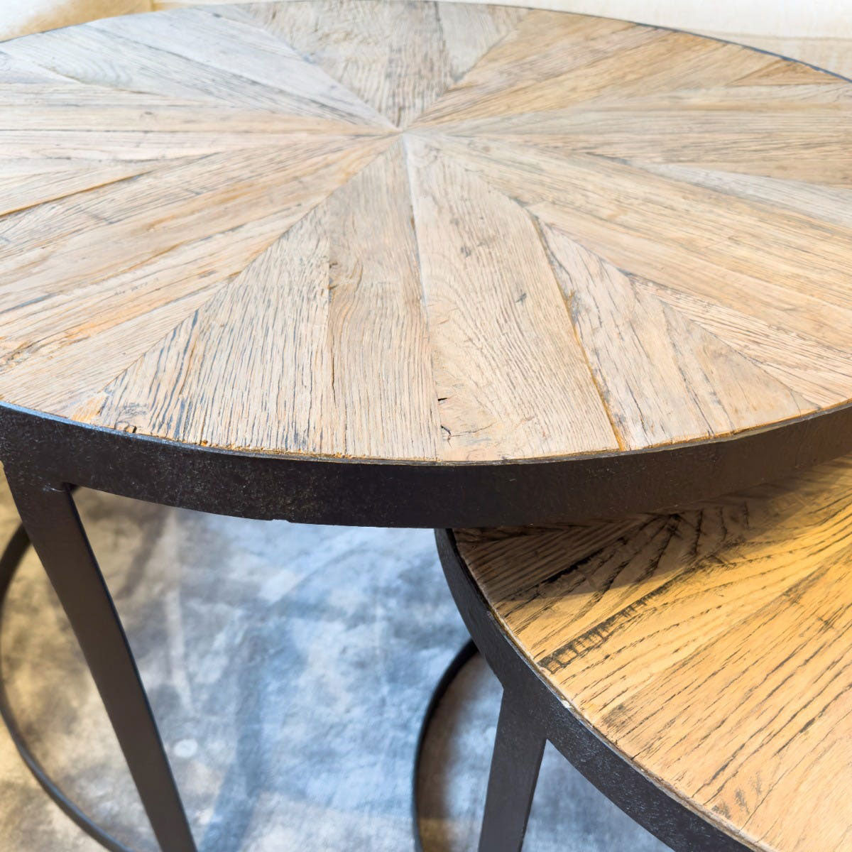 Round wooden coffee table with a black metal base on a wooden floor.