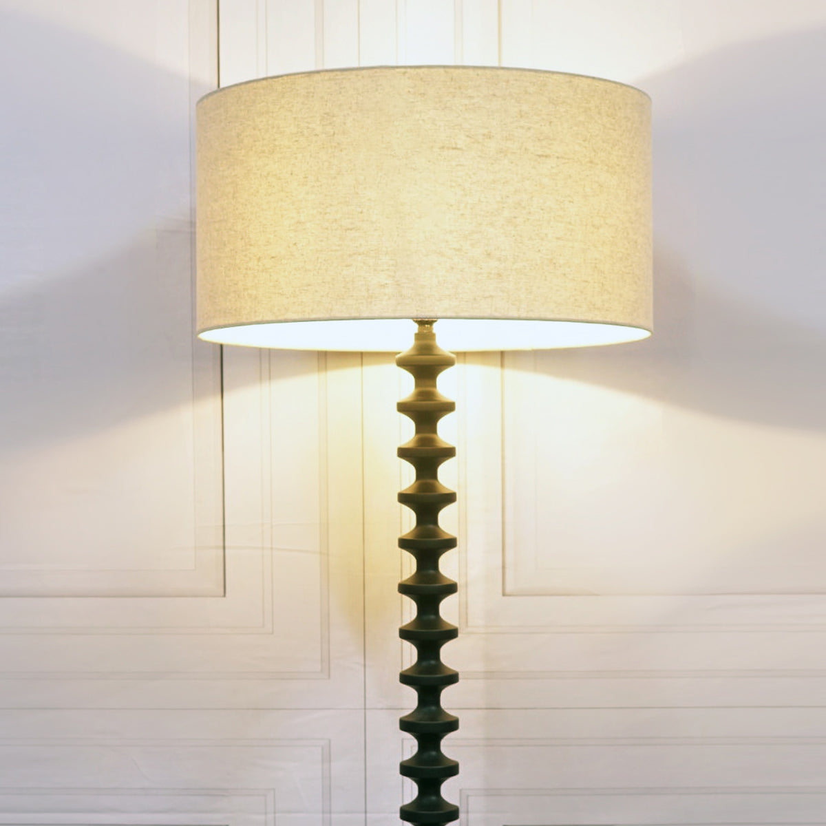 Floor lamp with a textured beige shade and decorative base against a neutral wall.
