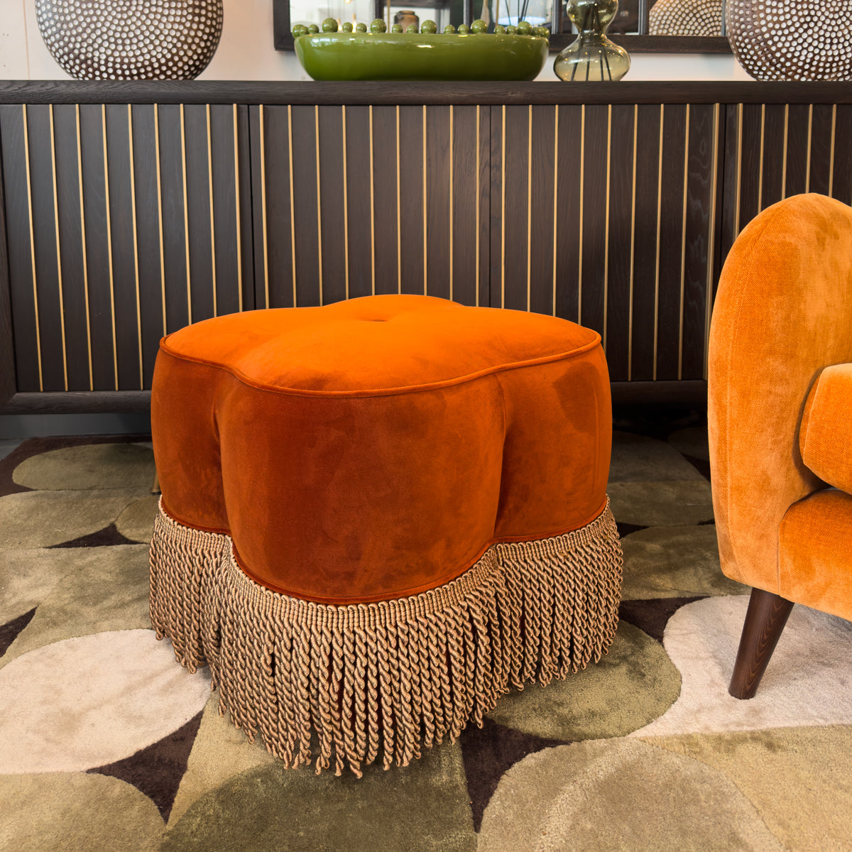 Orange ottoman with fringe base in a room setting