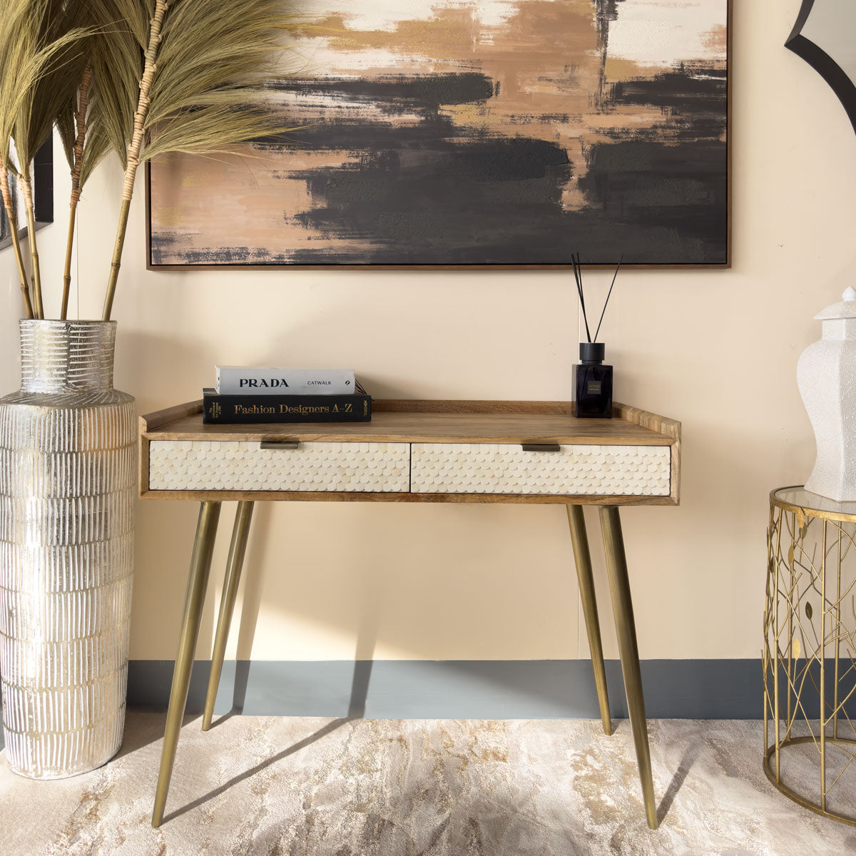 Decorative console table with Prada books, vase, and abstract painting in a stylish interior setting.