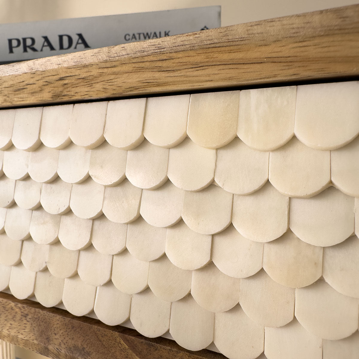 Console table with shell-like pattern and wooden frame, Prada book in the background.