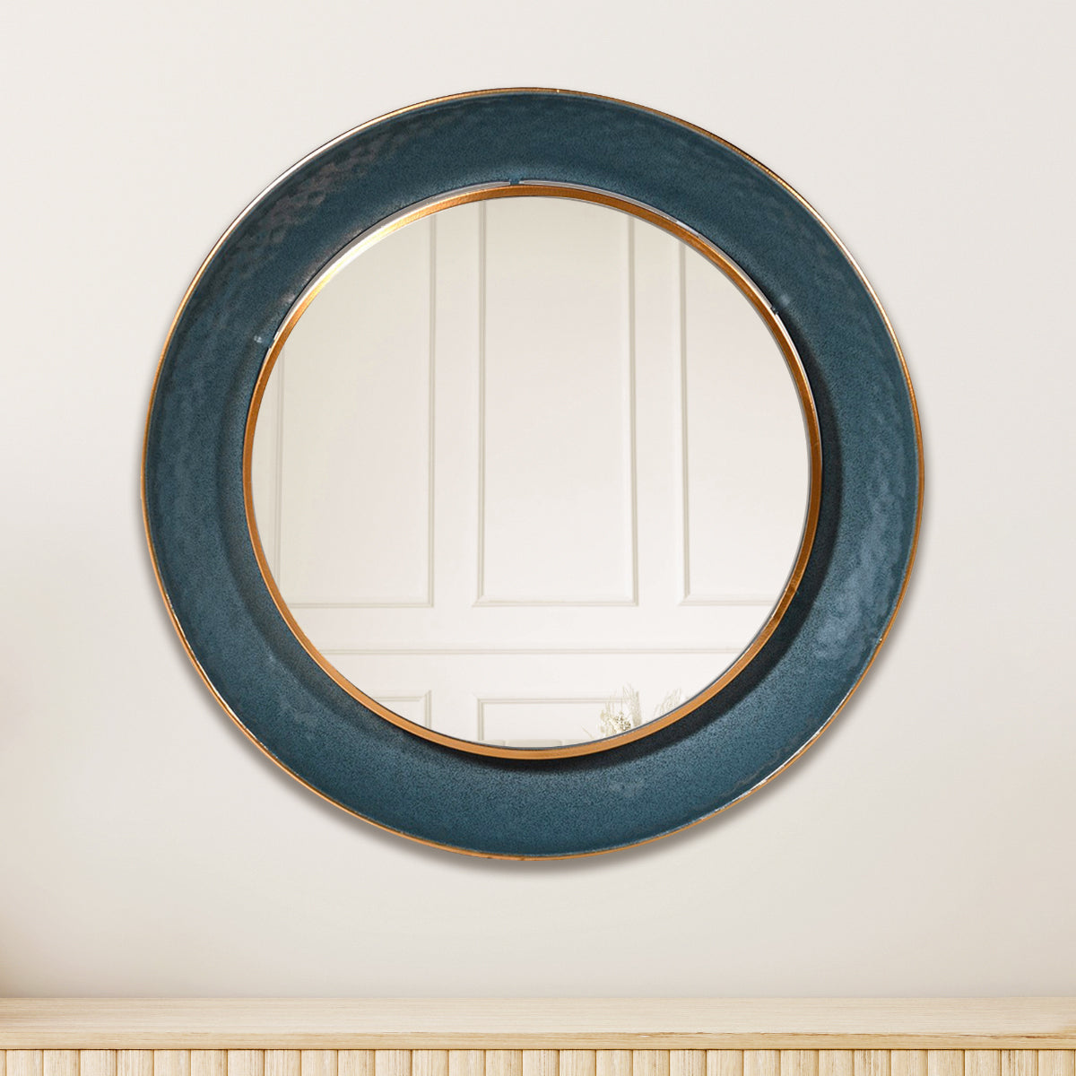 A teal and gold round wall mirror hanging above a ridged wooden sideboard.