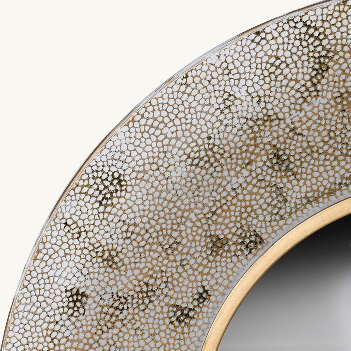 A close up of a gold and white textured mirror with a circular golden border around the mirror glass.