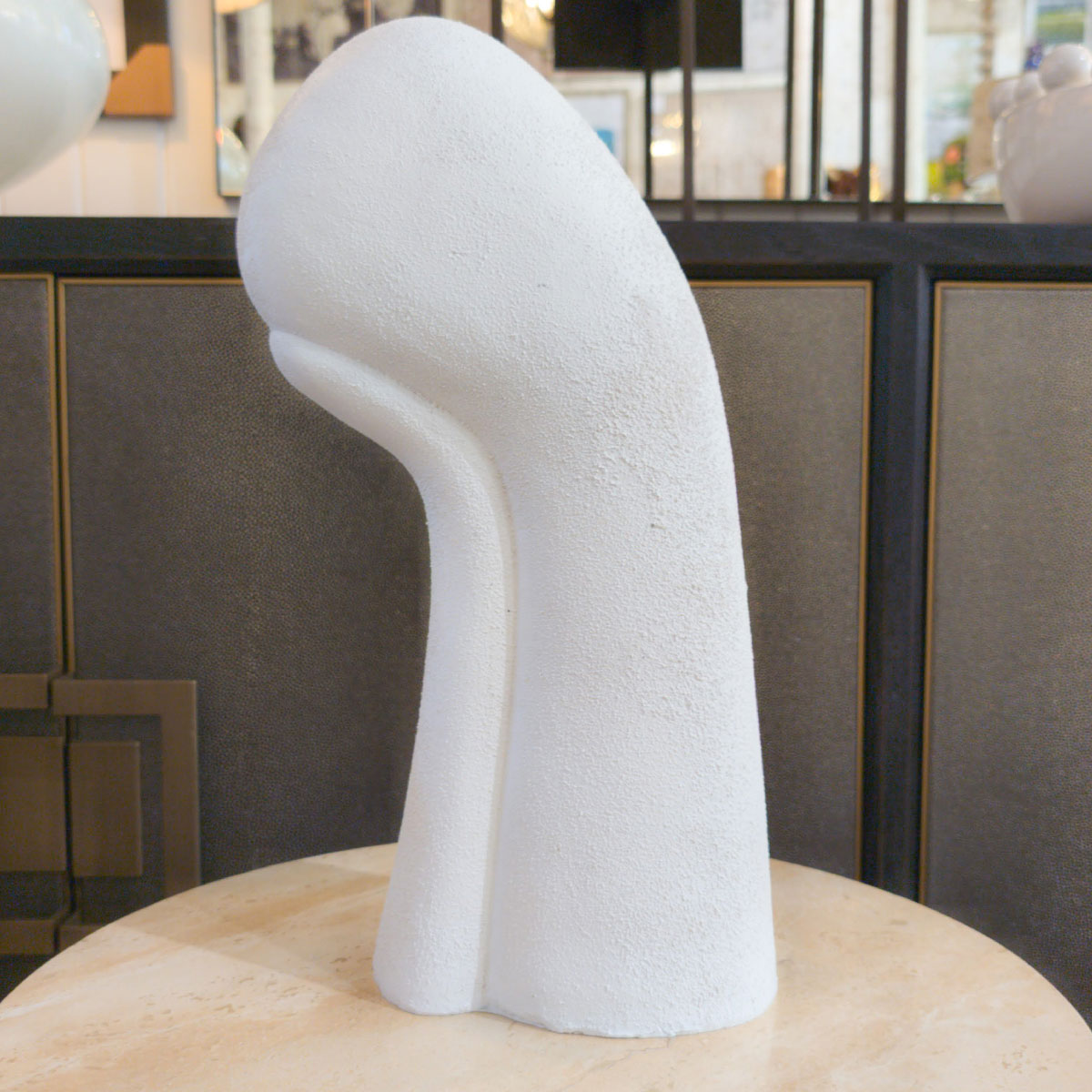 White abstract sculpture on a wooden base with a blurred indoor background