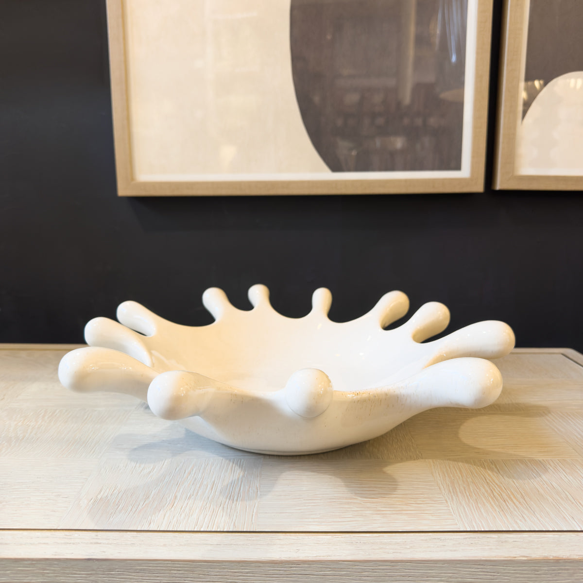 White abstract ceramic bowl on a wooden surface with framed artwork in the background
