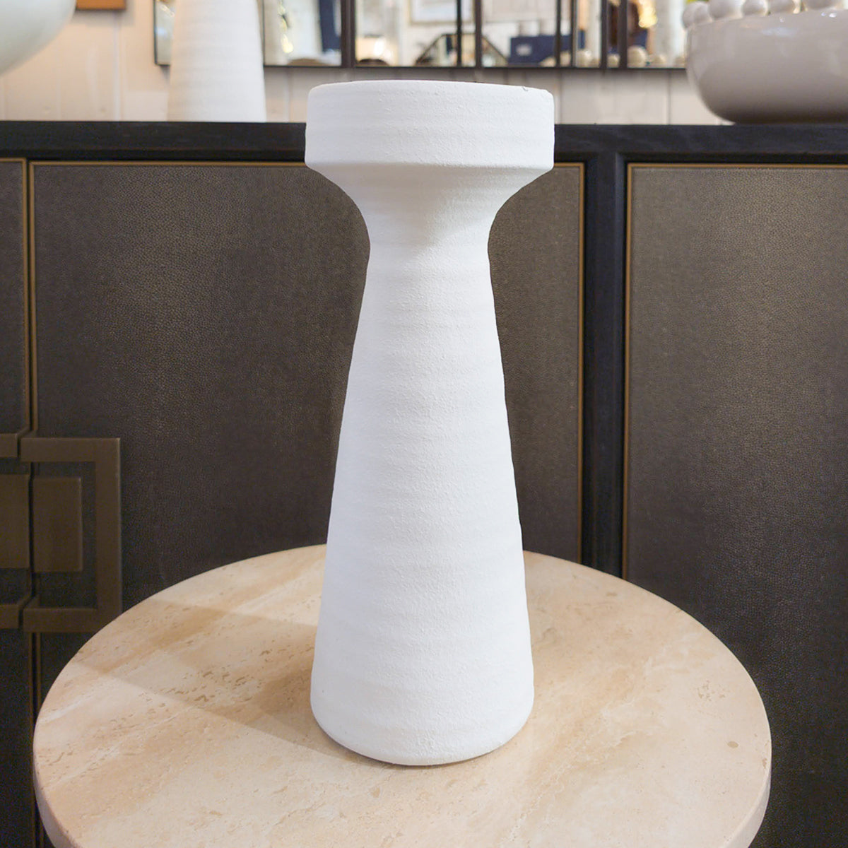 A white terracotta plaster look candleholder placed on a wooden surface, with a textured finish.