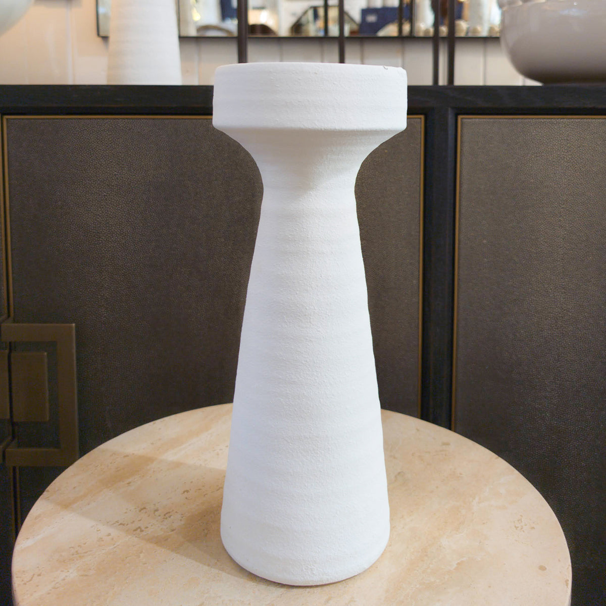 White plaster candleholder on a round beige surface with a dark sideboard in the background