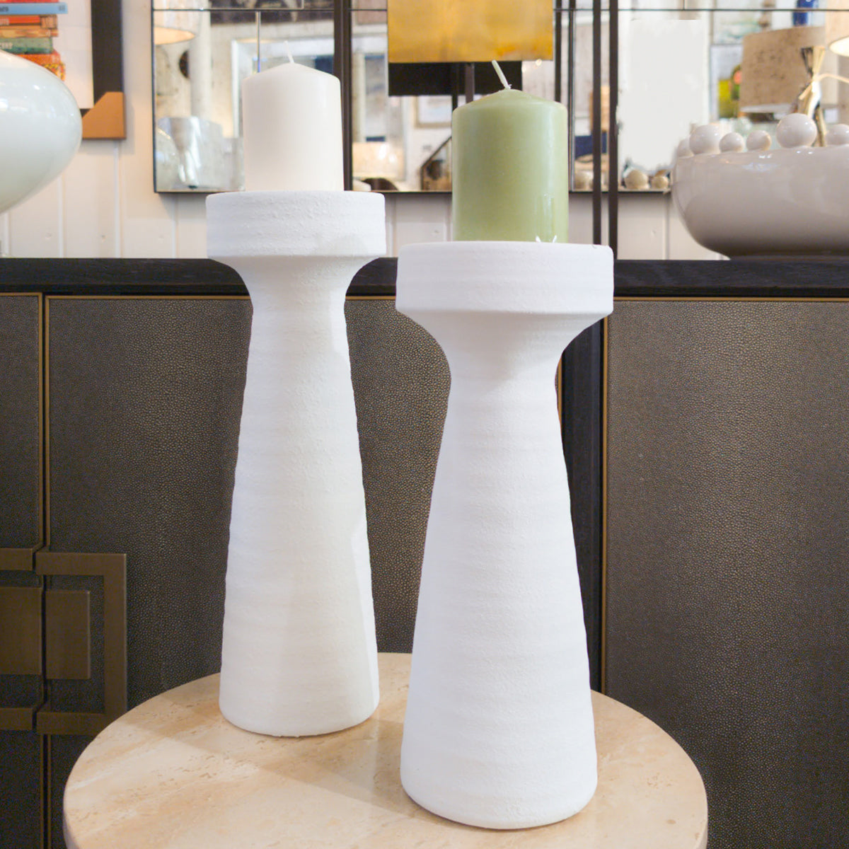 Two white cylindrical candlesticks on a wooden surface with a blurred background