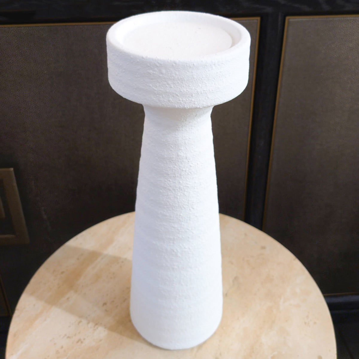 White textured pillar candleholder on a wooden surface with a dark background