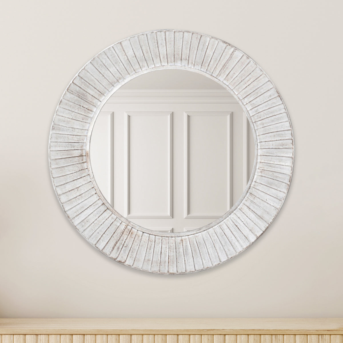 A white washed ridged iron wall mirror with a circular frame, hanging above a light wood slatted sideboard.