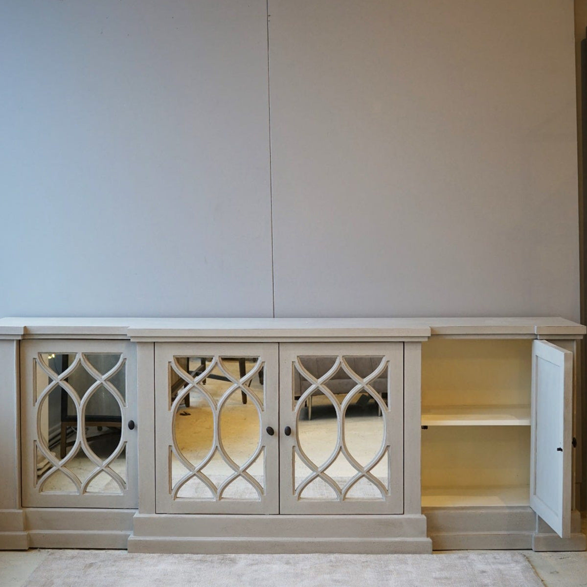 Light wood four door cabinet with decorative glass doors against a white wall.