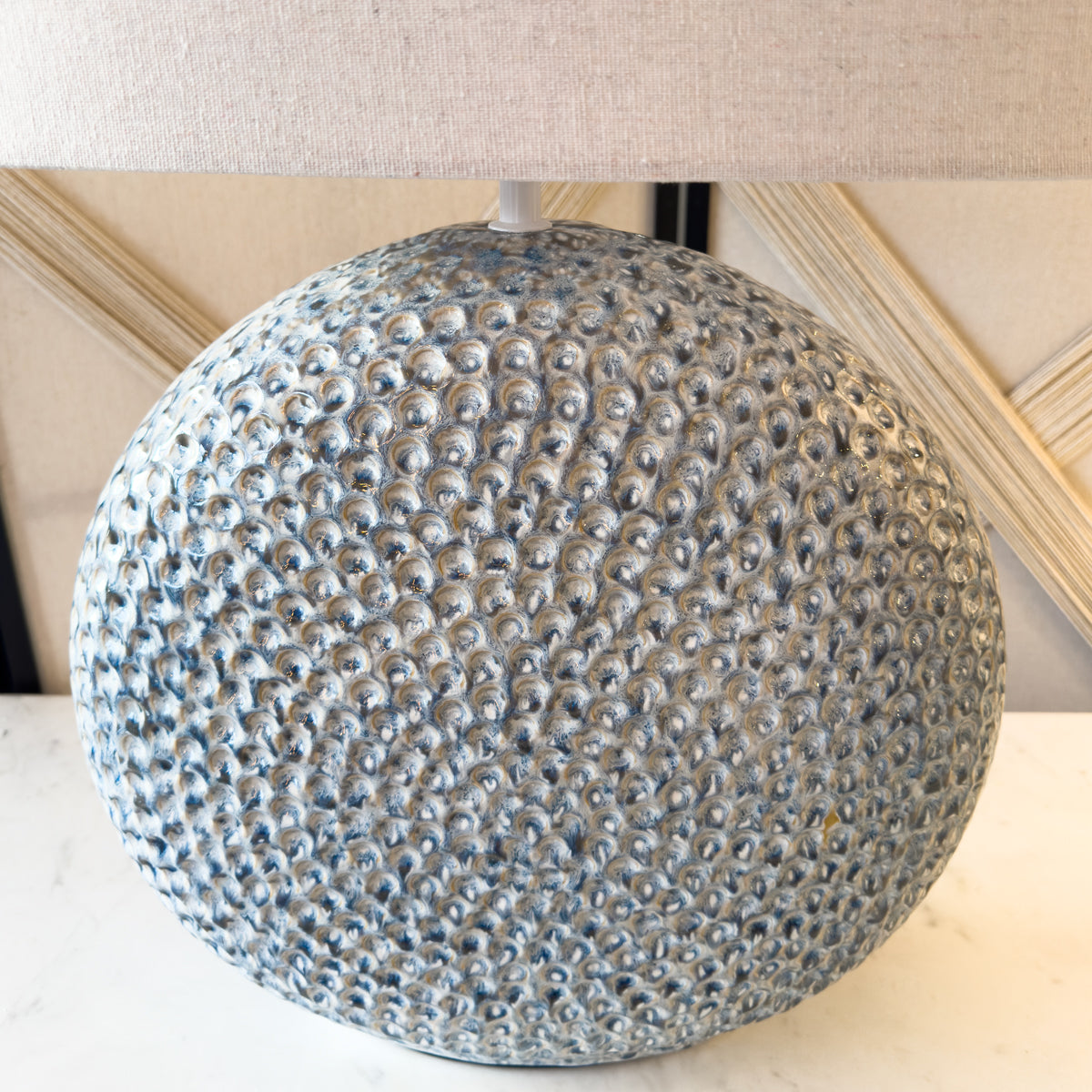 A close up of a round blue ceramic lamp with a white linen shade.