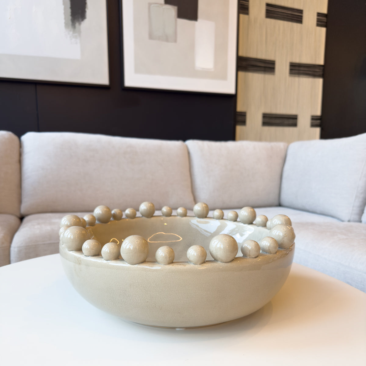 A cream bobble bowl sitting in a neutral coloured living room with abstract wall art on the walls.