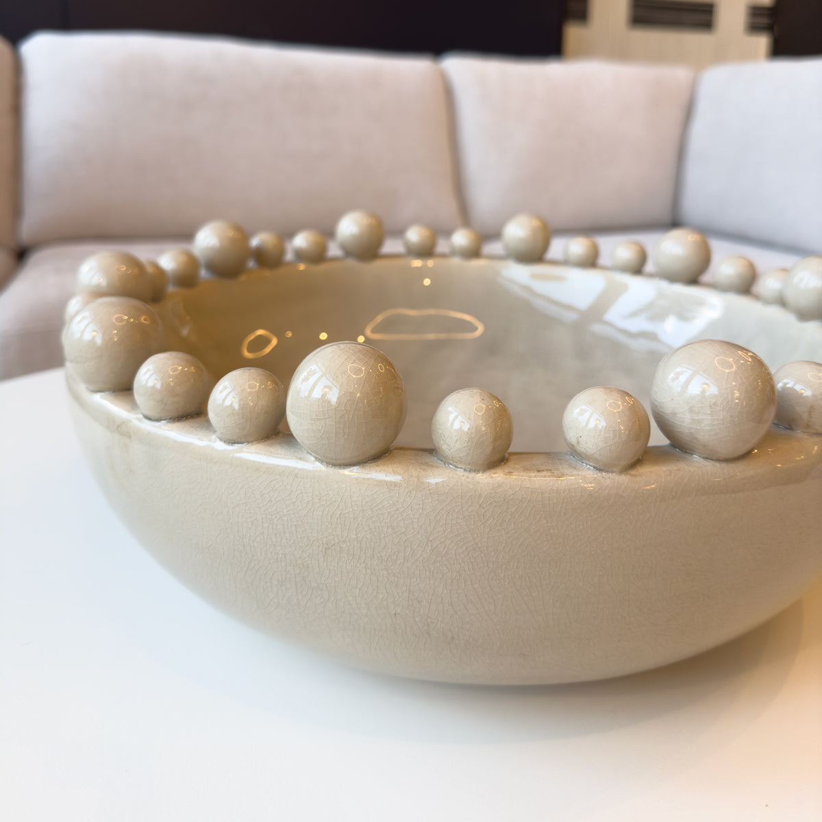 A cream ceramic bowl with ball surround, sitting on a coffee table.