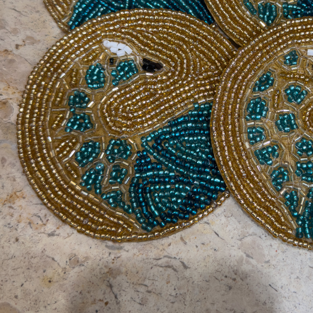 A close up of an ornate circular beaded gold coaster with gold peacock.