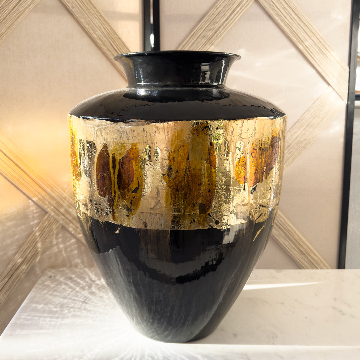 A high gloss black vase with a gold foil stripe, sitting on a white marble console.