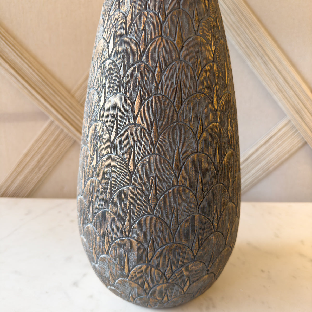 A close up of a art deco style table lamp with a grey base and gold scallop indentations.