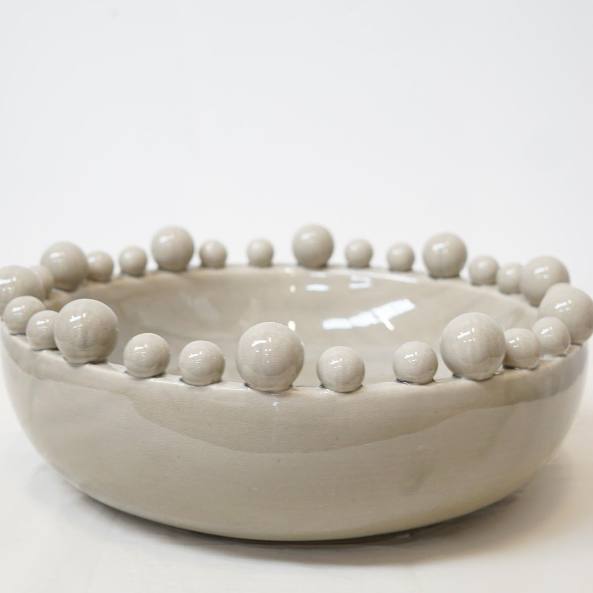 A pale grey ceramic decorative bowl with bobbles around the rim, sitting against a white backdrop.