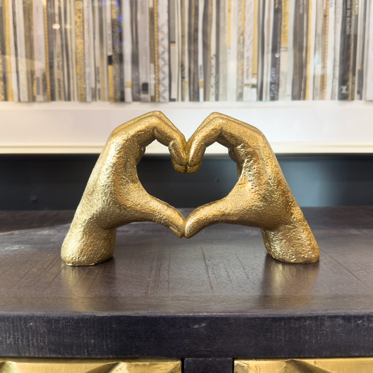 Gold sculpture of two hands forming a heart shape on a dark surface with a patterned background.