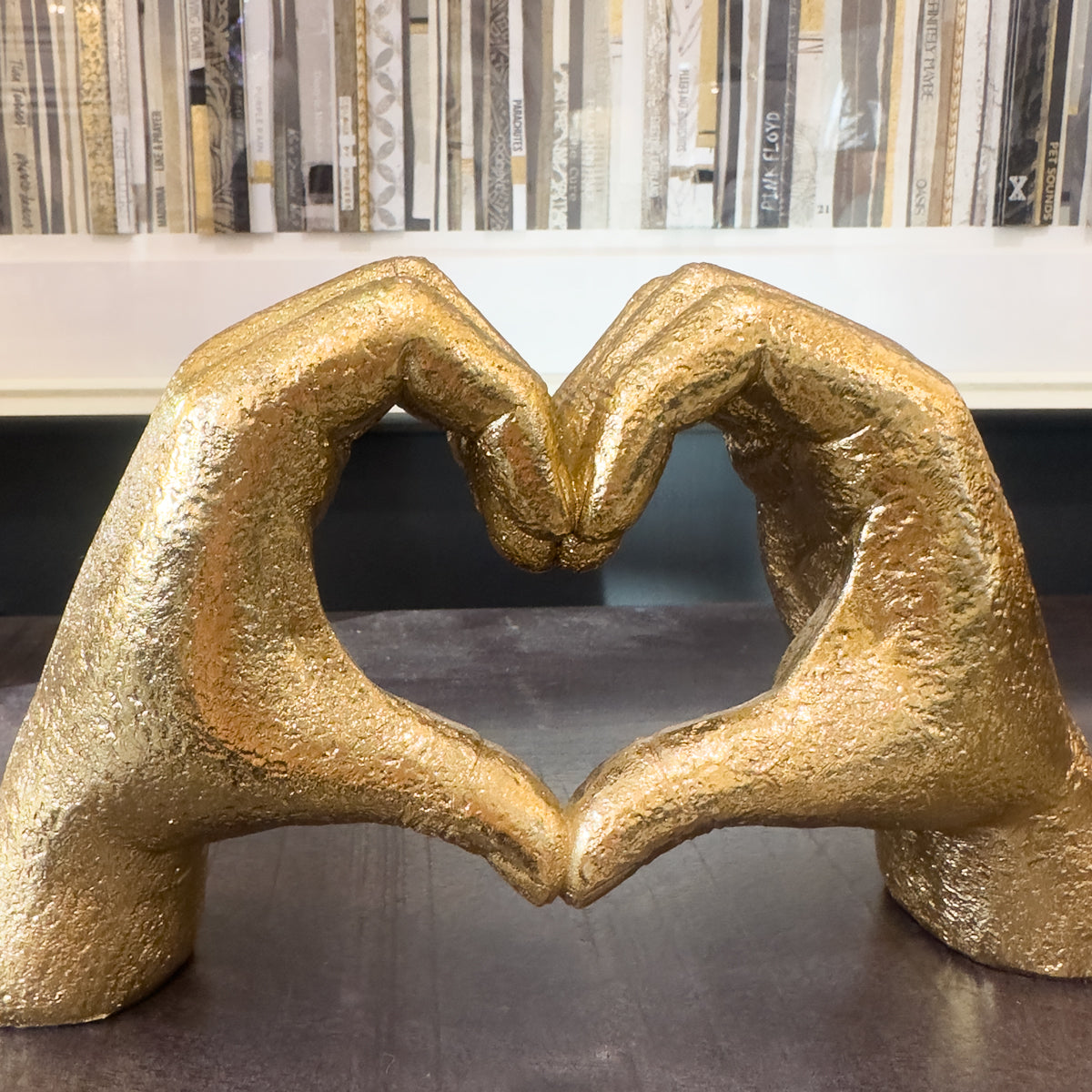 A gold heart hands sculpture on dark wood console table