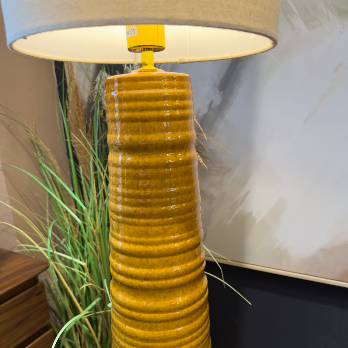 Close-up of a mustard-yellow ribbed ceramic table lamp with beige shade, beside ornamental grass, creating a warm, earthy interior mood.