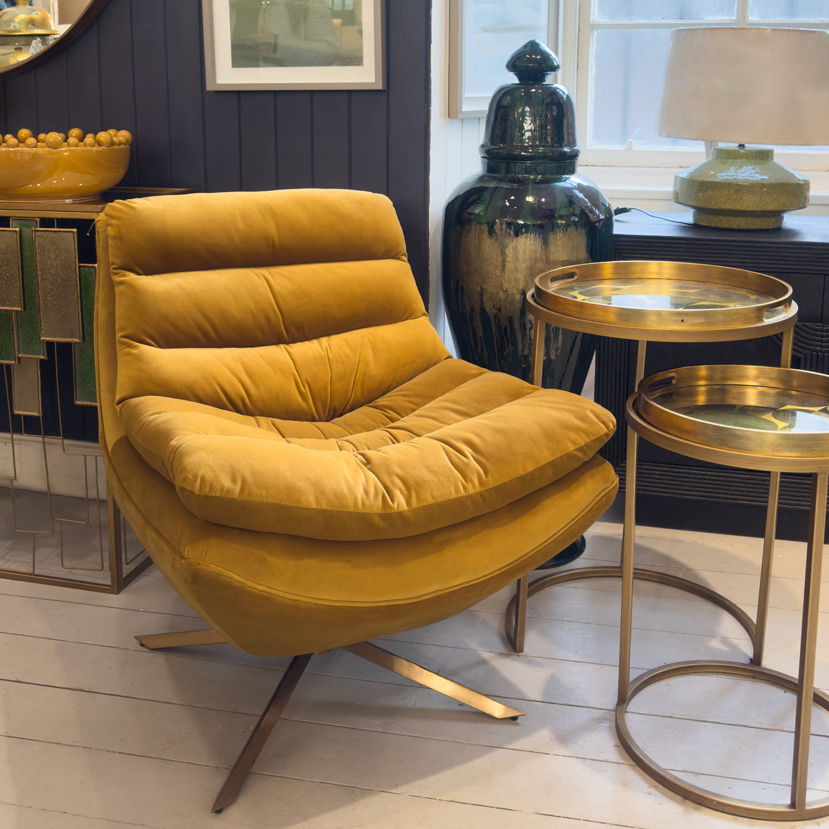 A mustard padded lounge chair next to gold nesting tray tables in a modern living room.