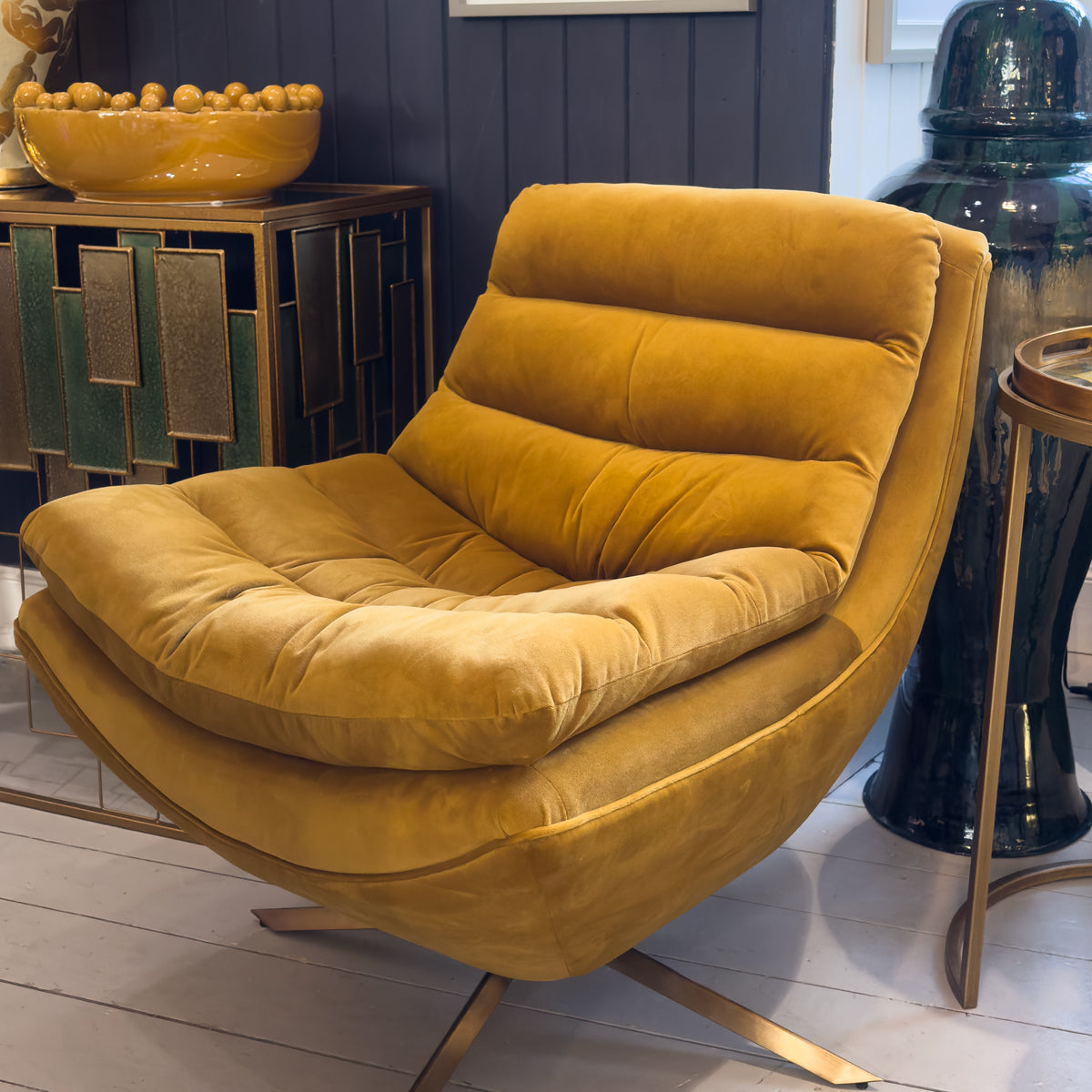 A mustard coloured velvet chair next to a green & gold panelled console table.