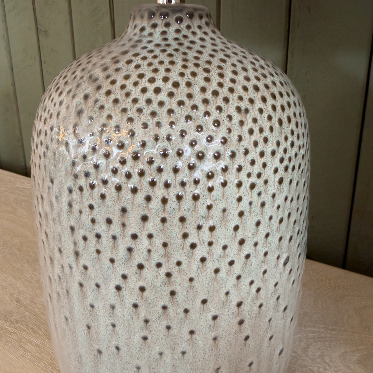 Close up of an olive ceramic lamp base with brown speckled details.