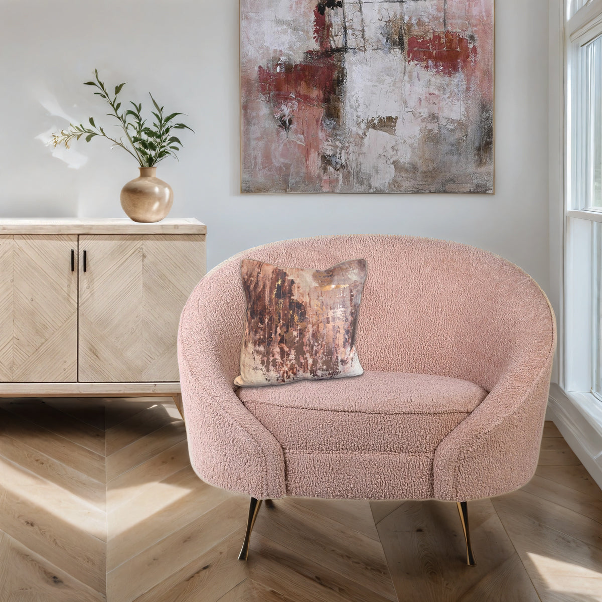 A pink boucle tub chair with distressed rose gold cushion, infront of a sideboard and a red & pink abstract canvas.