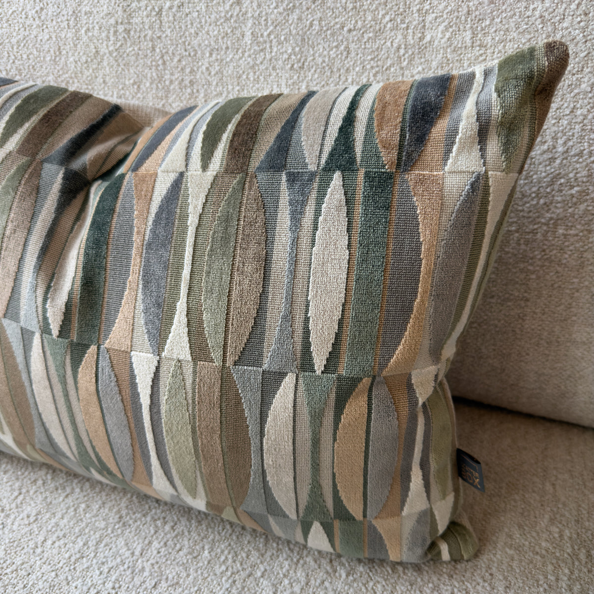 Decorative throw pillow with geometric vertical stripes in muted sage, beige, gray, and brown, resting on a textured neutral sofa.