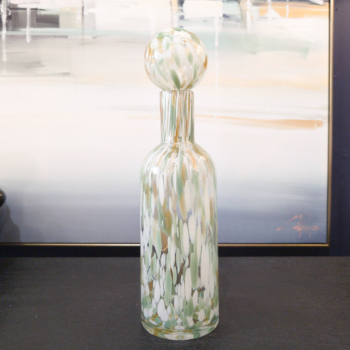 A green, white & gold glass bottle vase sitting on a black hallway table.