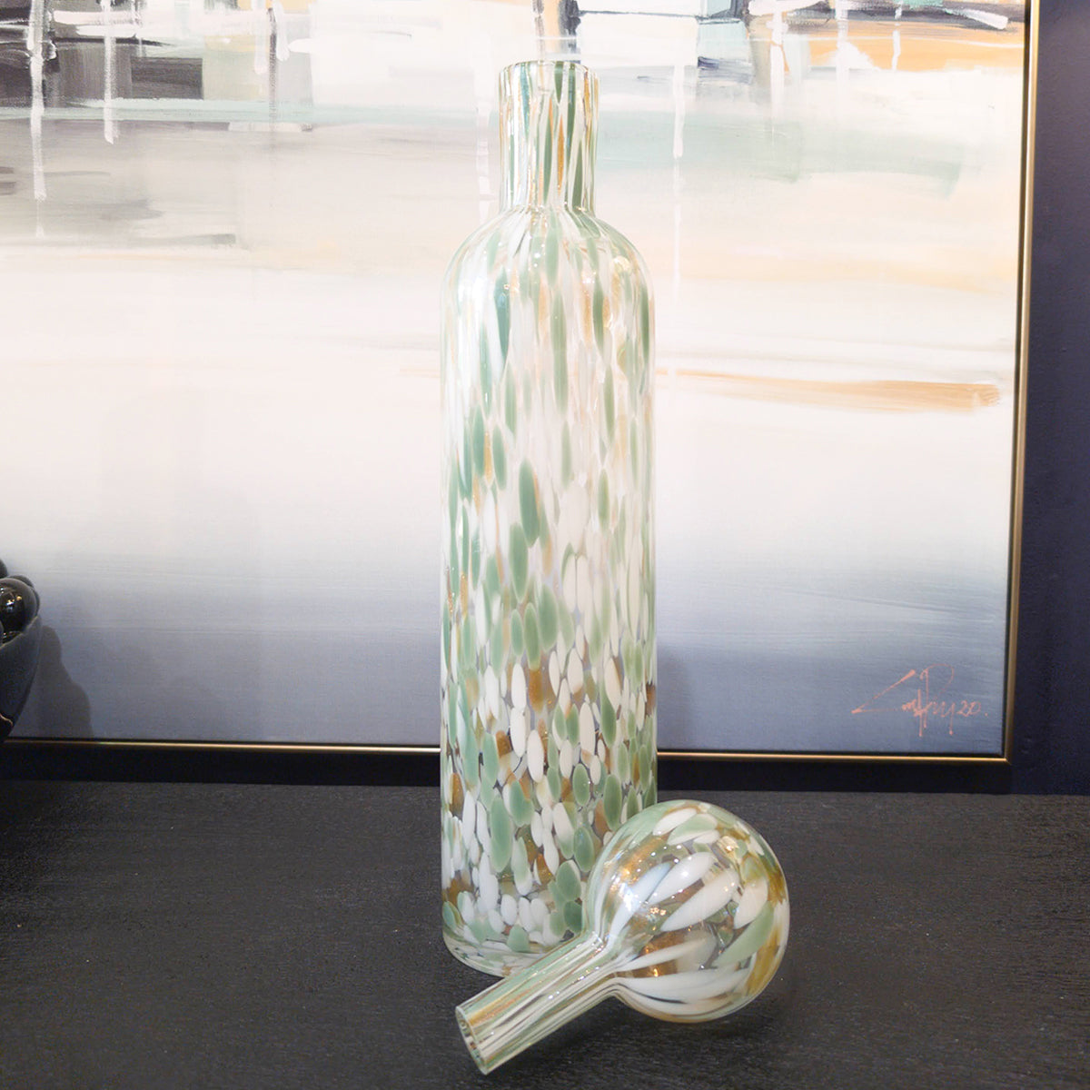 A lidded jar, sitting atop a black console table infront of a coastal wall art picture.