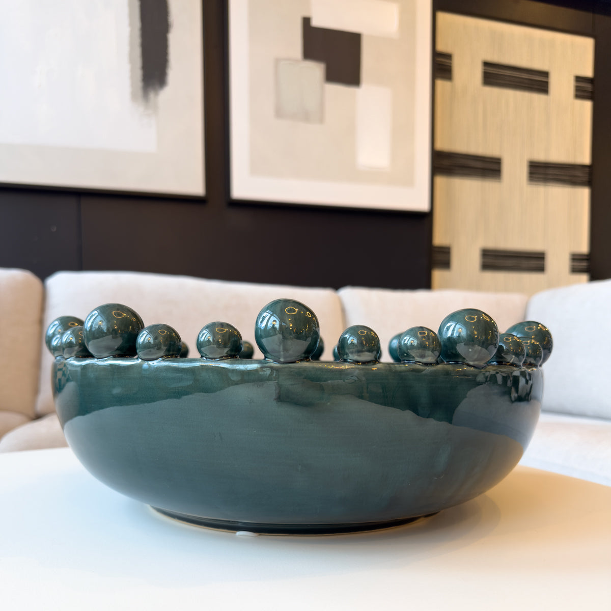 A teal coloured decorative bowl with ceramic bobbles around the rim, sitting on a coffee table in a living room.