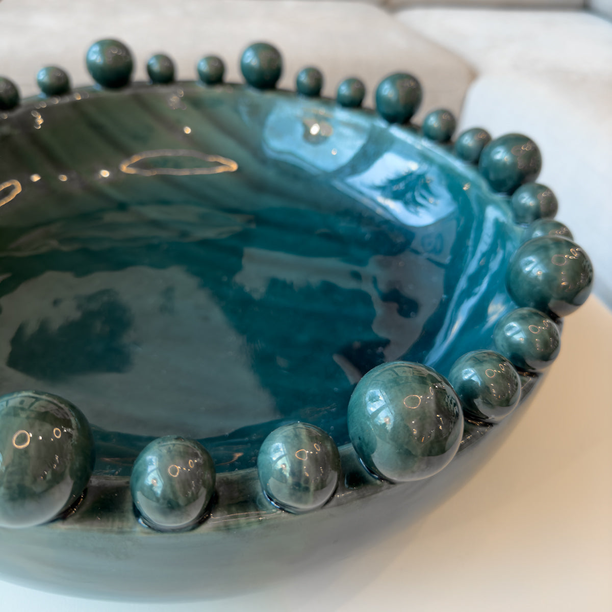 A close up of a glossy teal ceramic bowl for home decoration, sitting on a white table.