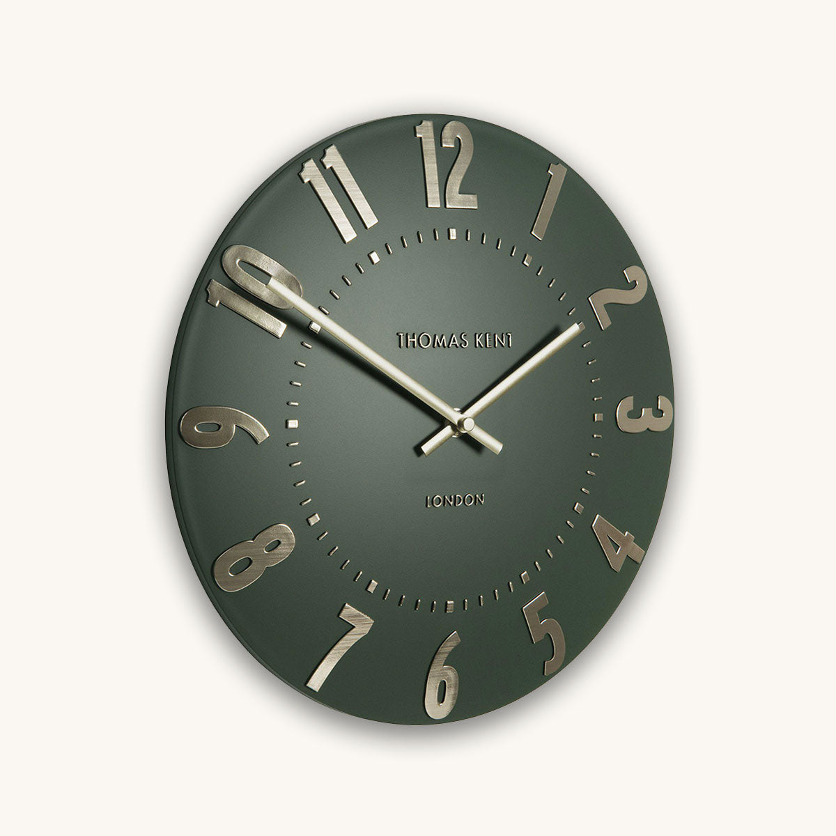 Green wall clock with gold numbers and brand name on a white background
