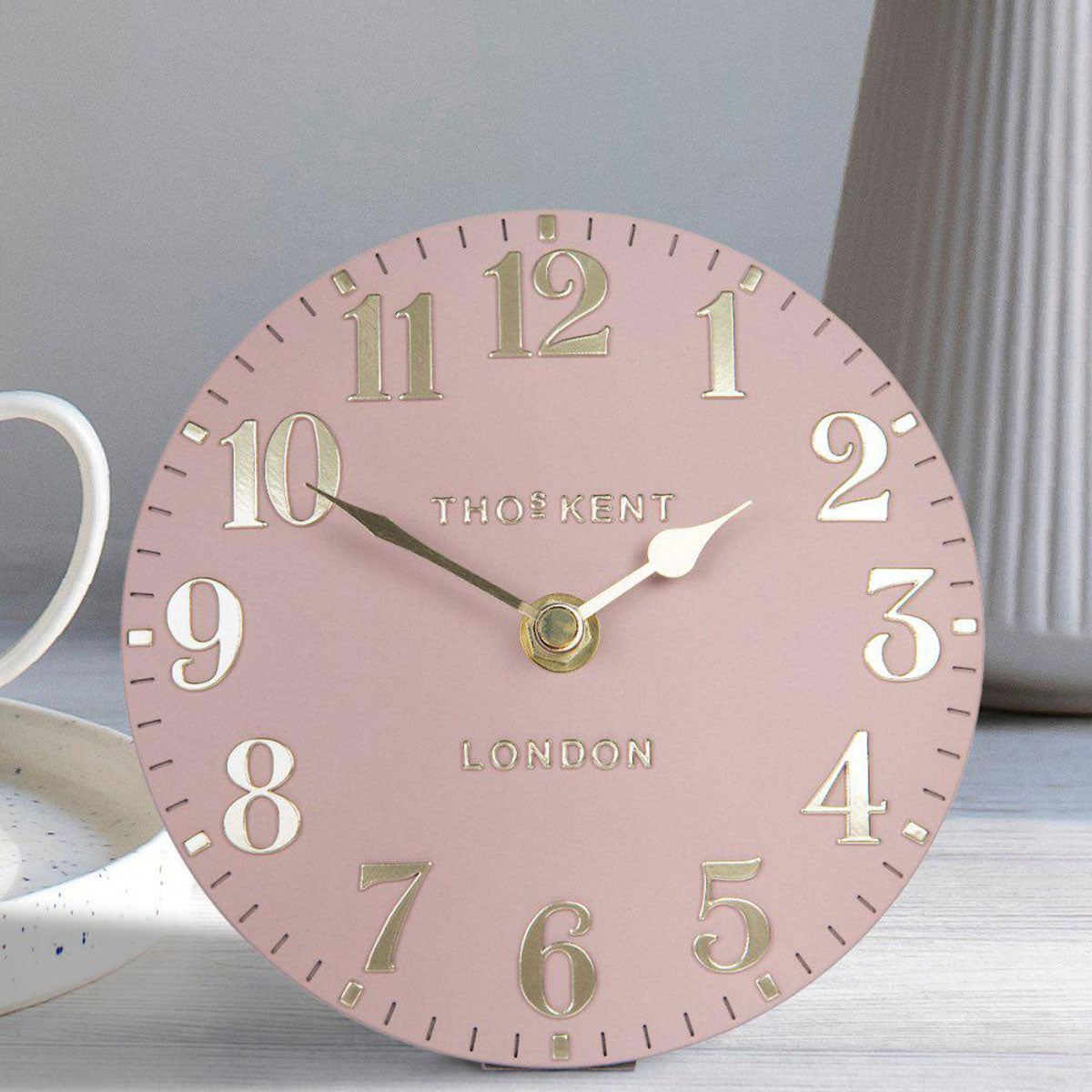 Pink clock with gold numbers and 'Thos. Kent London' branding on a light surface.