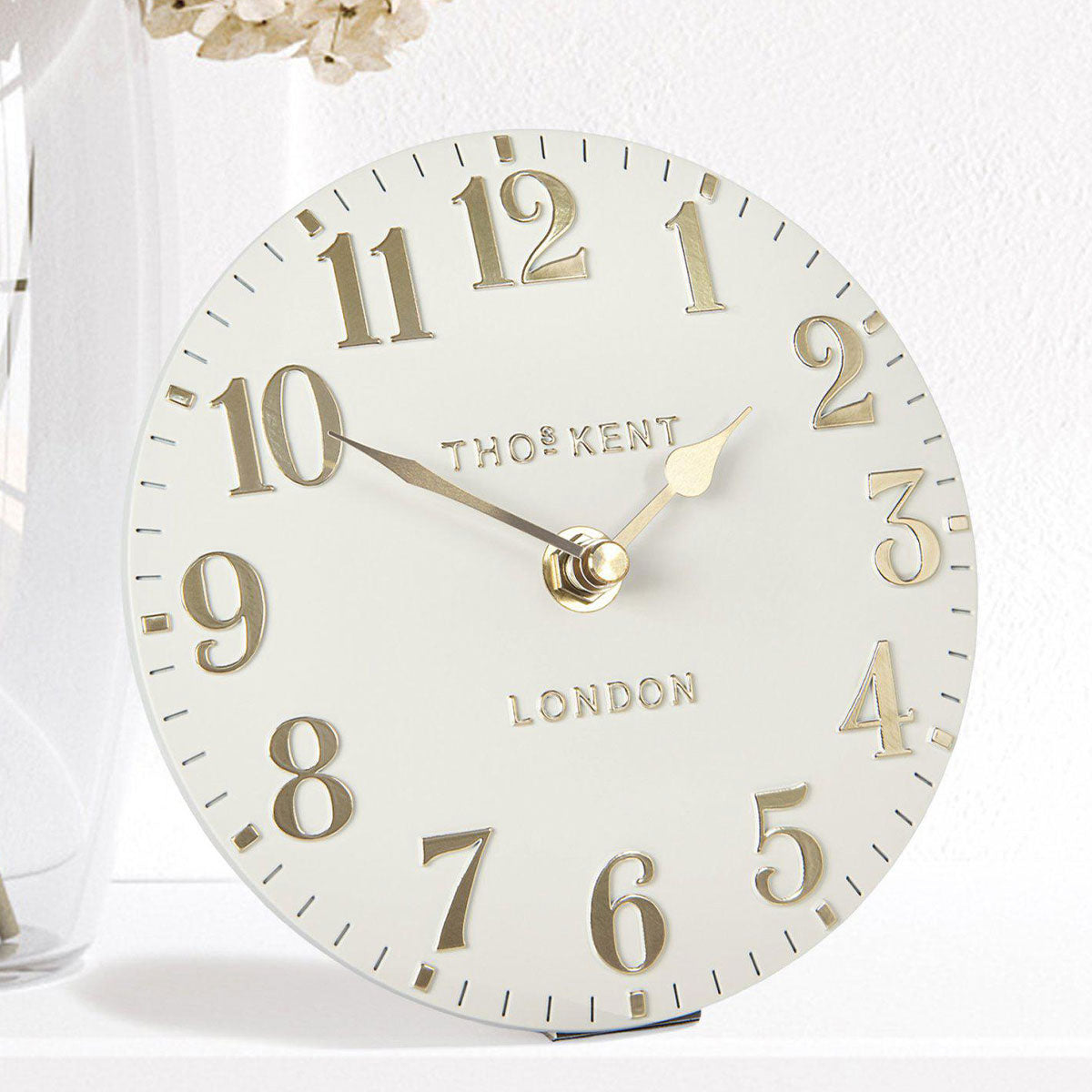 White clock with gold numbers and 'Thos. Kent London' branding on a white background