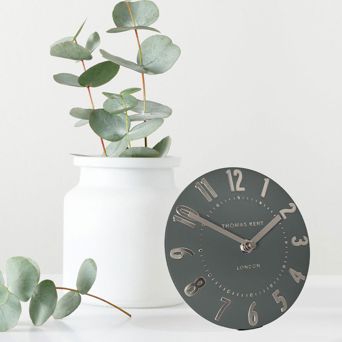 Round mantel clock with white vase and green plant on a light background