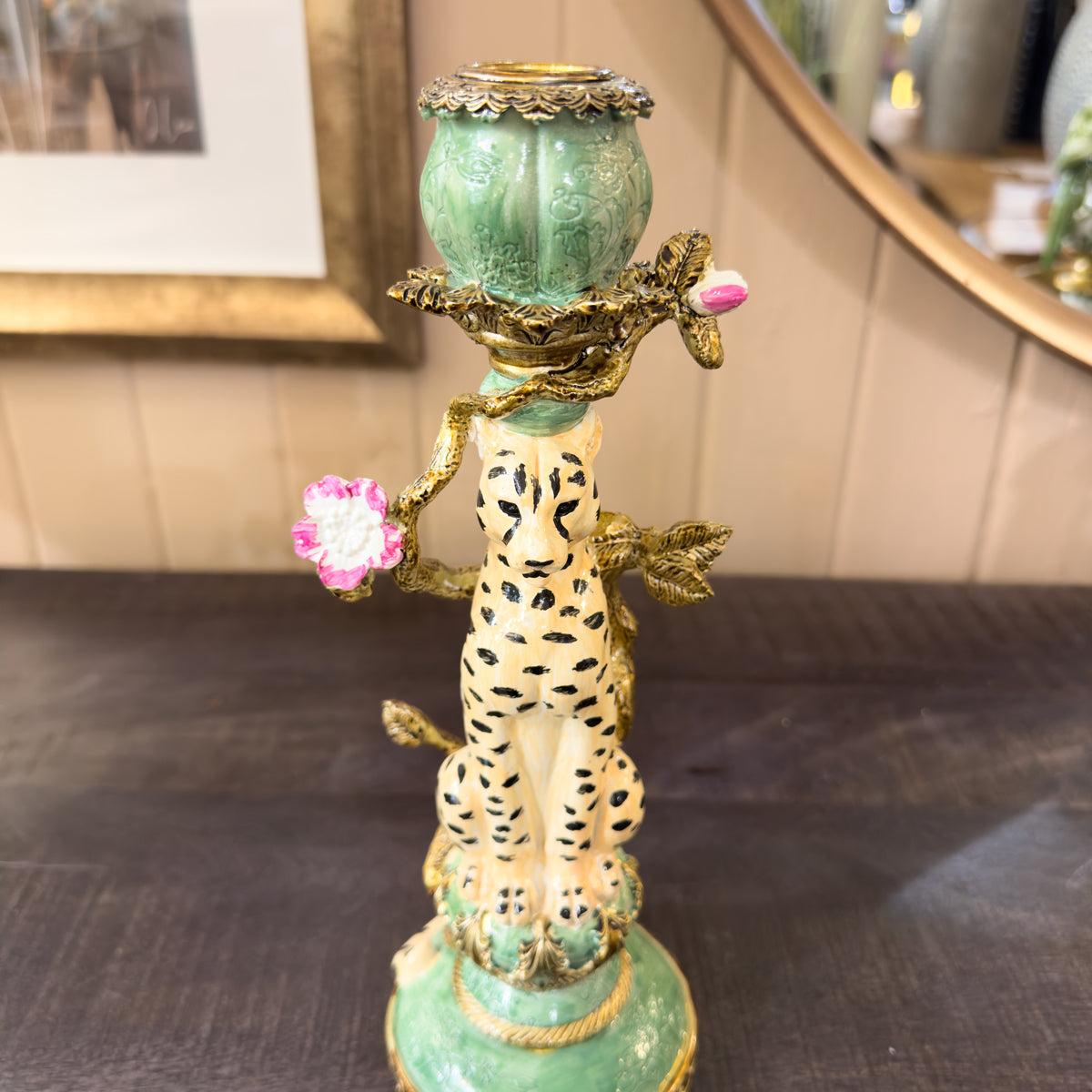 Decorative candle holder with leopard design and floral elements on a wooden tabletop surface.