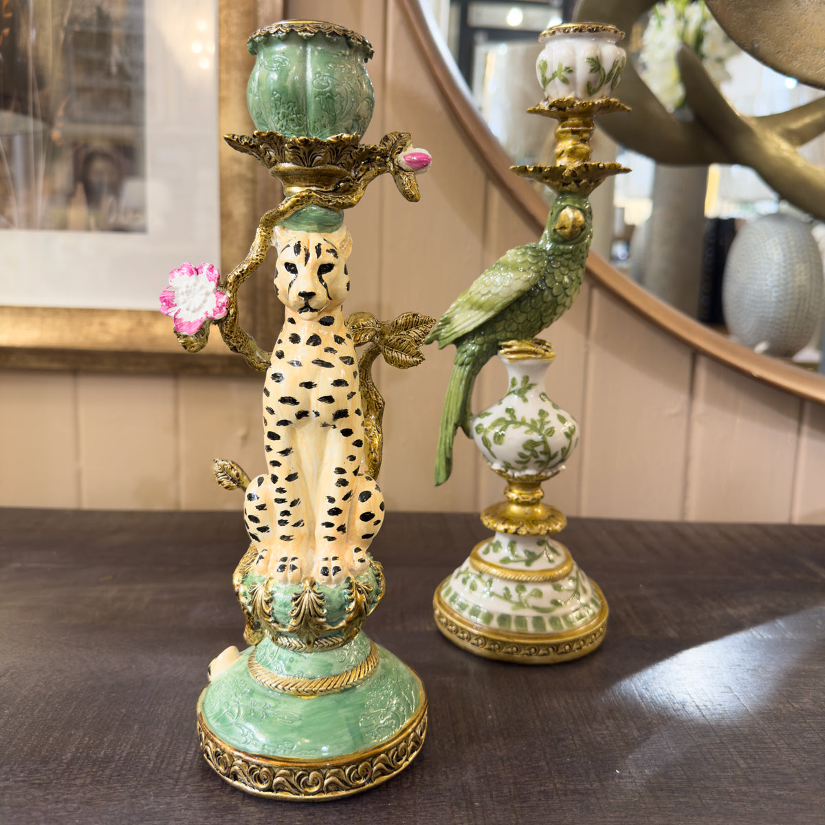 Green candle holder with cheetah and parrot design on a wooden sideboard surface.