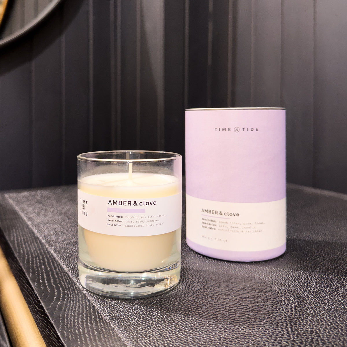 Candle and its packaging labeled 'Amber & Clove' on a dark surface.