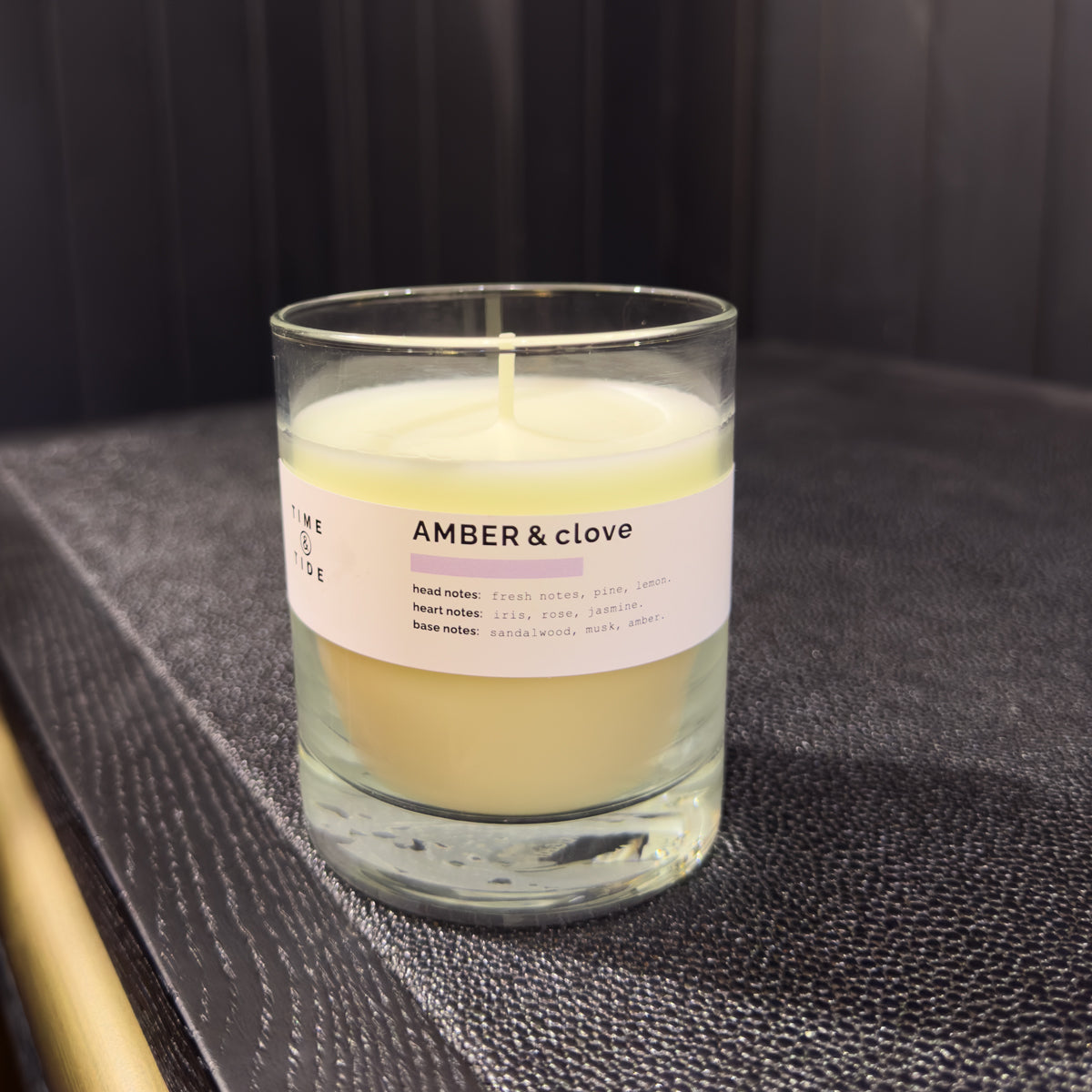 Candle labeled 'Amber & Clove' on a textured surface with a dark background