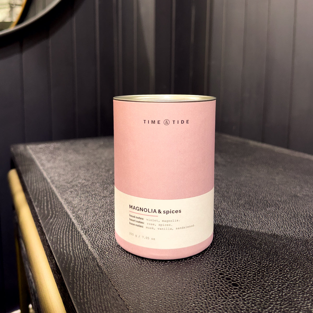 Pink cylindrical container labeled 'Time & Tide' on a dark surface